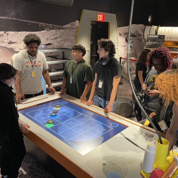 Students gather around a tabletop video game.