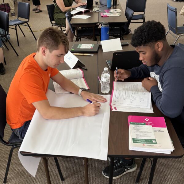 Students sitting at a table, studying facts about teen mental health.