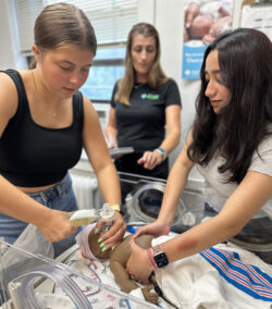 Two female students practicing CPR on a baby doll