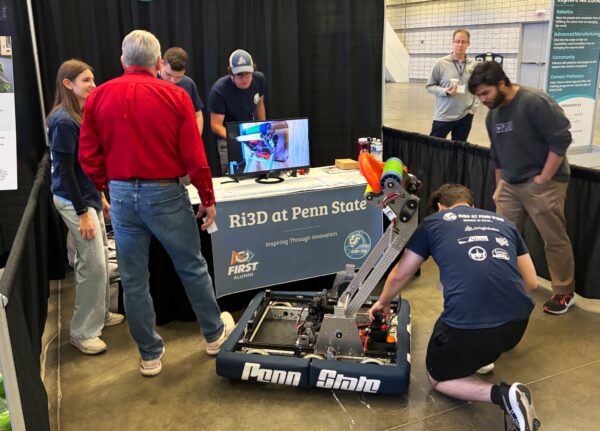 Penn State students kneeling and standing around RiD3 booth and robot at Robotics Day