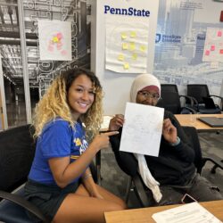 Two female students hold a paper with notes written on it