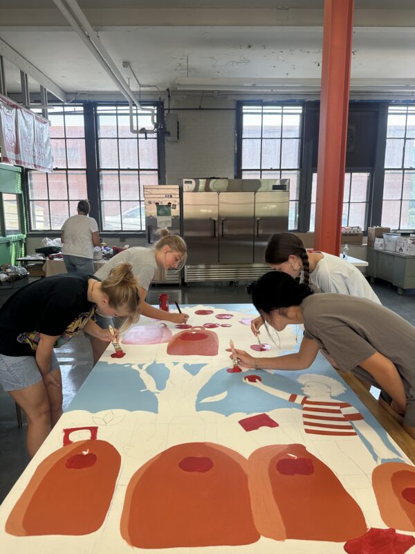 four students painting board mural for Cambria County Backpack Project