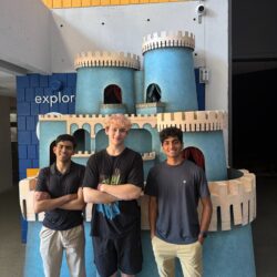 Three students stand in front of a blue model of a castle.