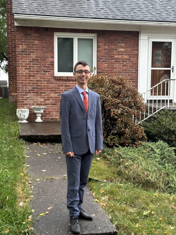 Stephan in a suit standing in front of a house