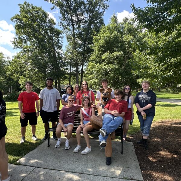group of students sitting on and standing by bench with sitting lion mascot statue at Penn State Altoona