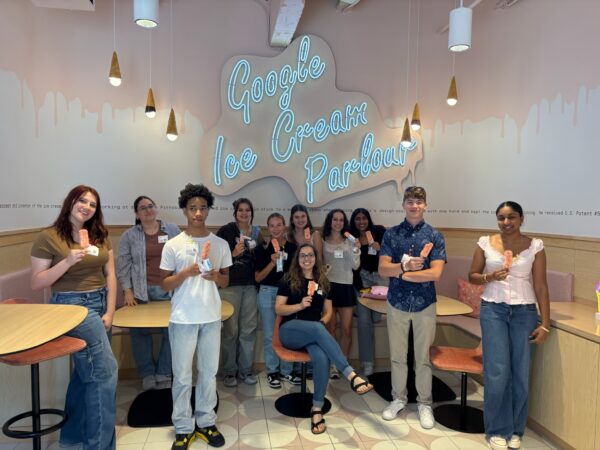 Group of students standing in front of Google Ice Cream Parlor neon sign eating ice cream