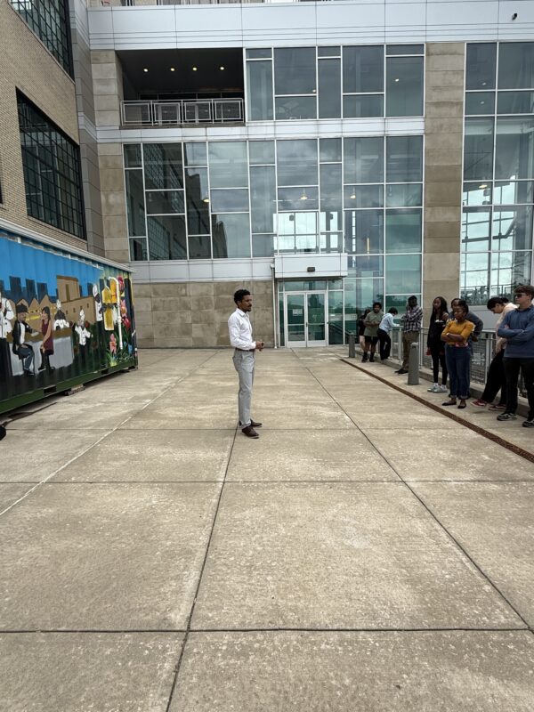 Kyle from Ecotone standing in front of group of students on one side and ZEUS digester on other side