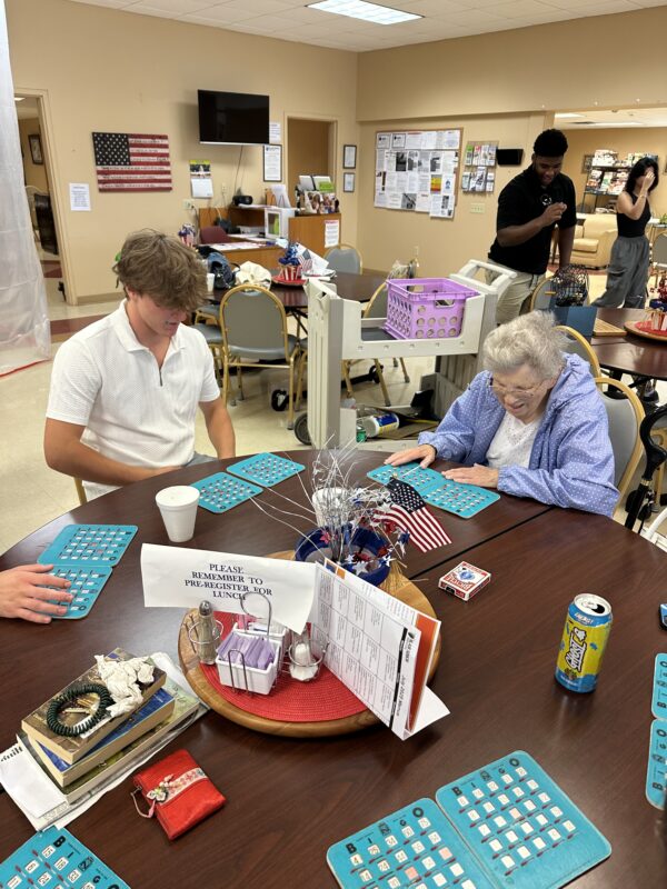 student sitting with senior citizen playing bingo at Blair Senior Services during community service day