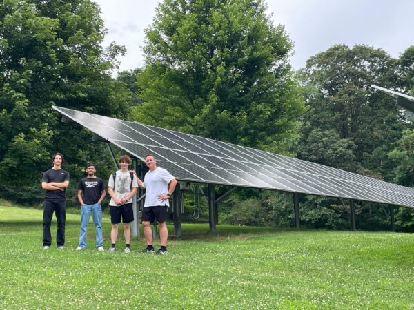 two students and instructor standing in field in front of big solar banners - deer lakes park