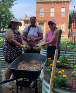 Volunteers standing with a wheelbarrow full of dirt while planting flowers in a community garden