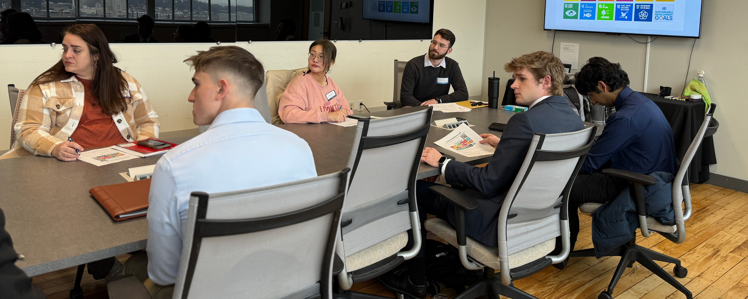 Group of six people around a table with a tv monitor displaying sustainable development goals